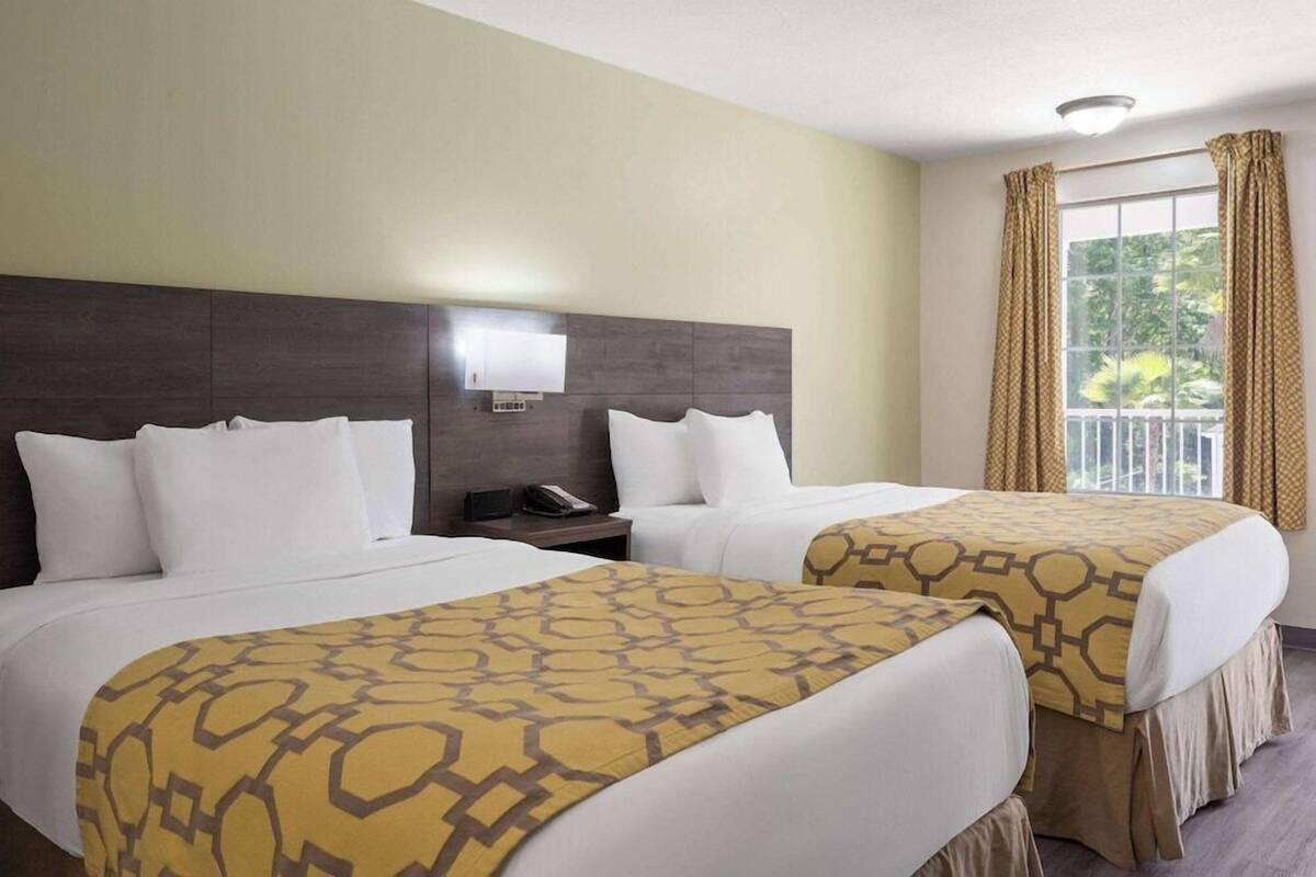 Une chambre d’hôtel avec deux lits, une table de chevet, une lampe et une fenêtre avec des rideaux.
