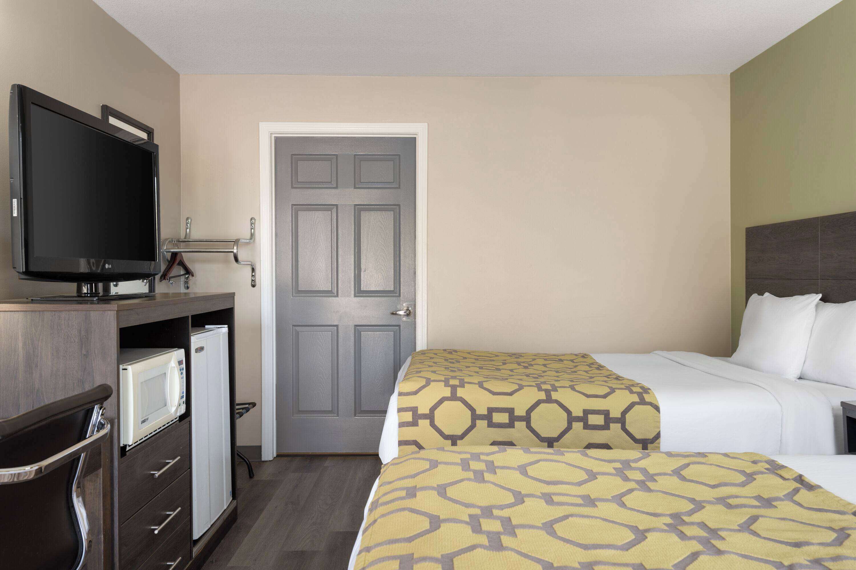 A hotel room with a bed, a TV, a mini-fridge, and a door.