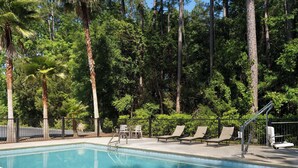 Una piscina con sillas de descanso y una mesa, rodeada de árboles altos.