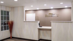 Zona de recepción con un letrero de 'Baymont', un mostrador de recepción, una puerta y una ventana con vistas.