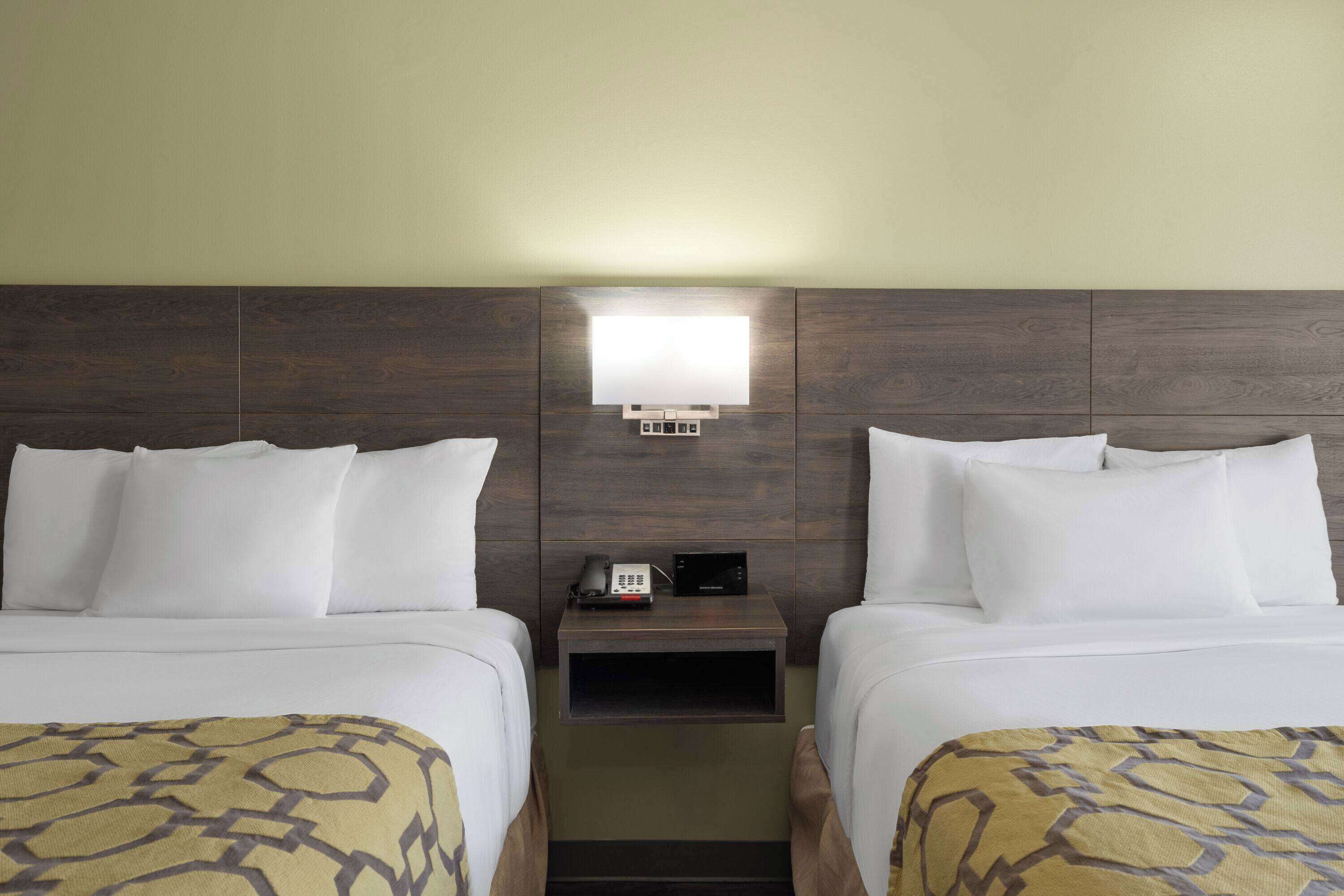 A hotel room with two beds, a nightstand with a lamp, and a wall-mounted TV.