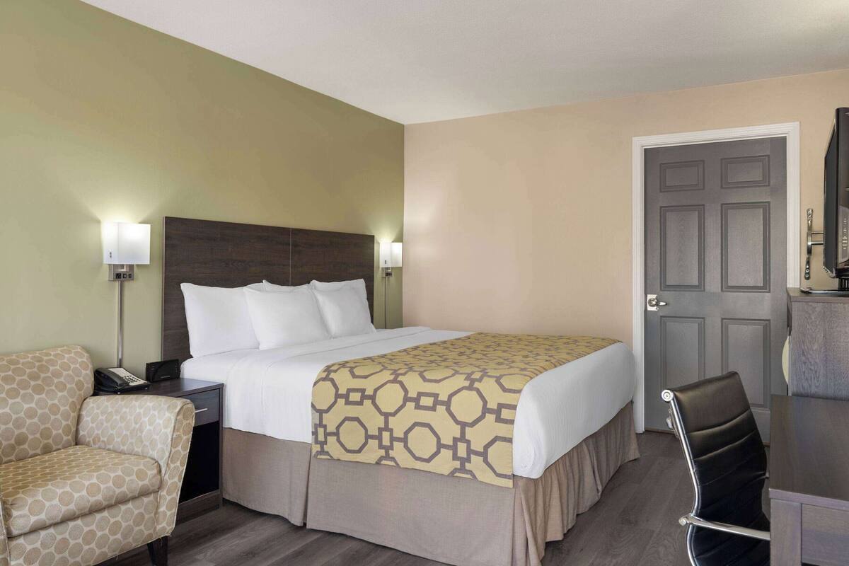 Une chambre d’hôtel avec un lit, une chaise, un bureau et une porte.