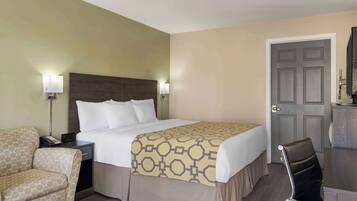 A hotel room with a bed, a chair, a desk, and a door.