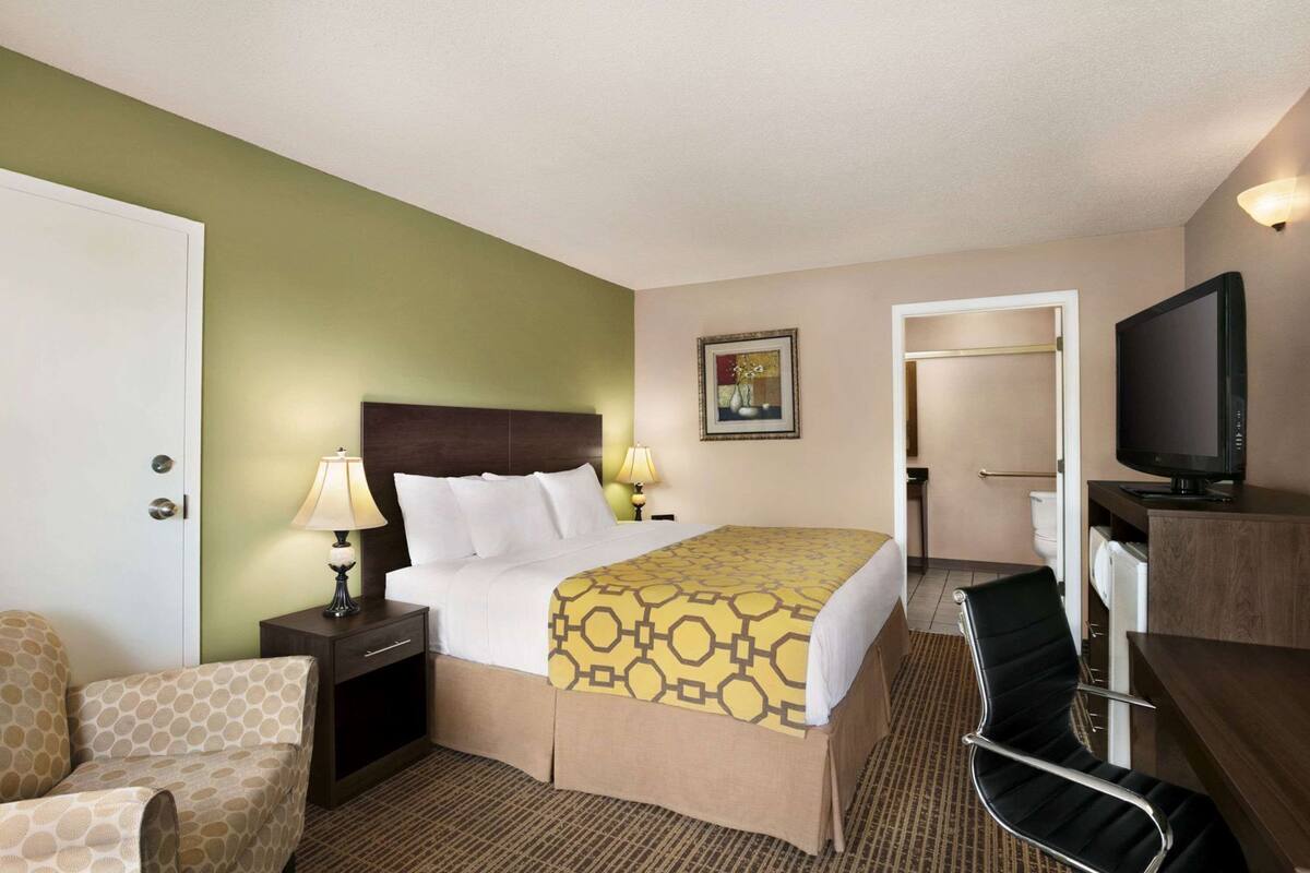 Une chambre d’hôtel comprenant un lit, des lampes de chevet, un bureau avec une télévision, une chaise et une porte donnant sur une salle de bain.