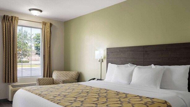 Una habitación de hotel con una cama grande, una mesita de noche, una lámpara y una ventana con cortinas.