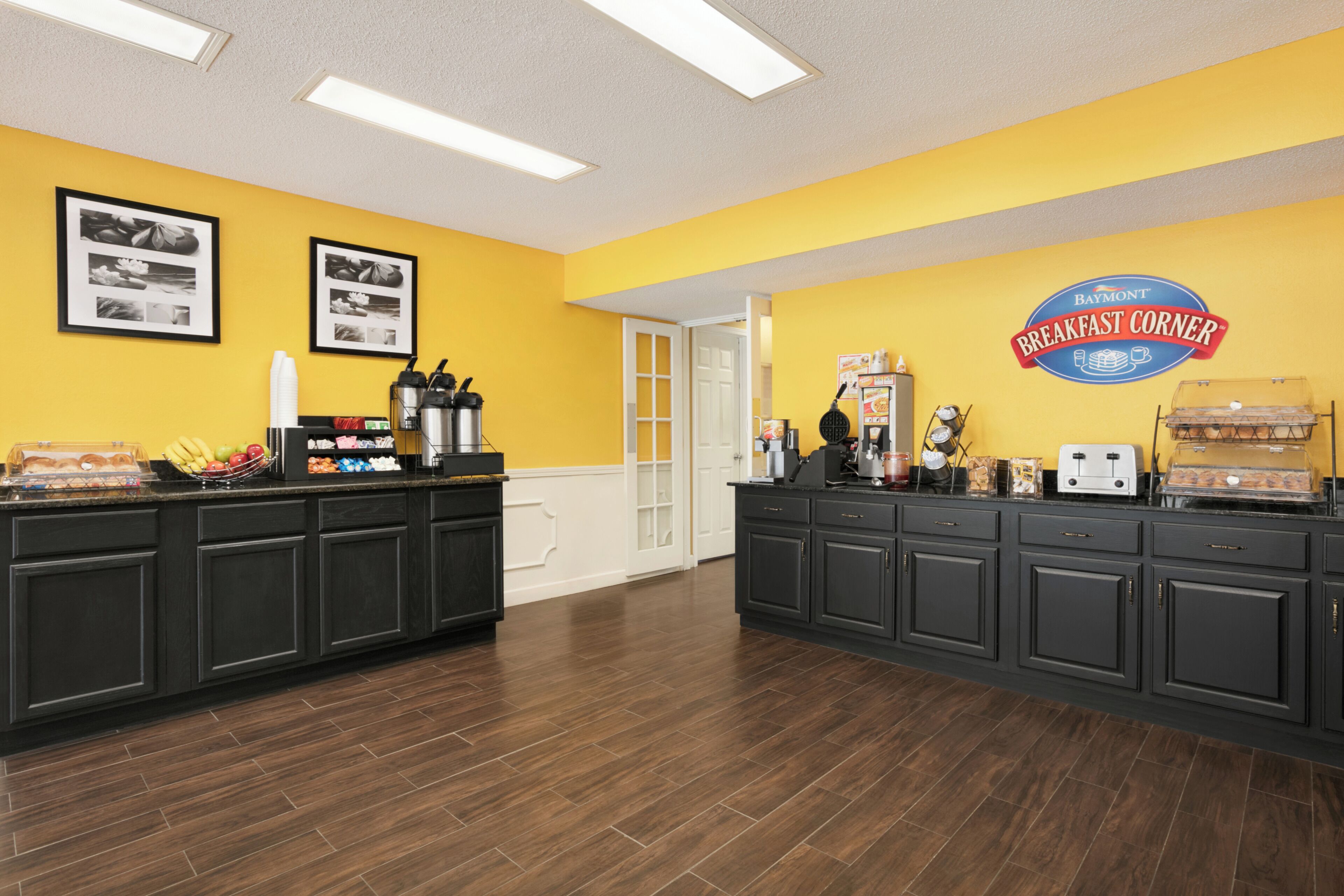 A breakfast area with a counter, coffee machines, and a sign for Baymont Breakfast Corner.