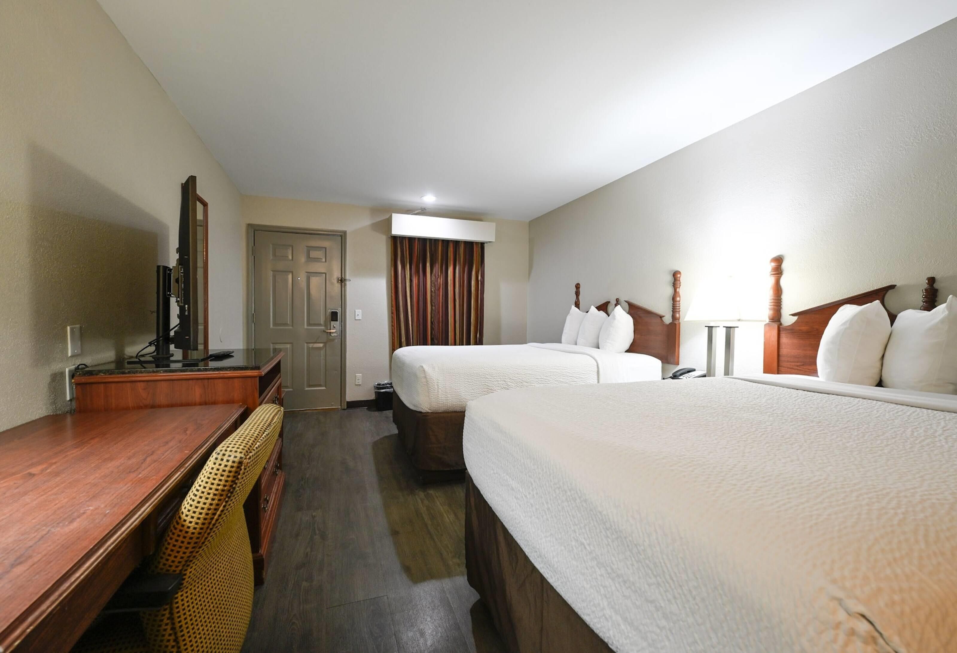 A hotel room with two beds, a desk, a chair, a mirror, and a door.