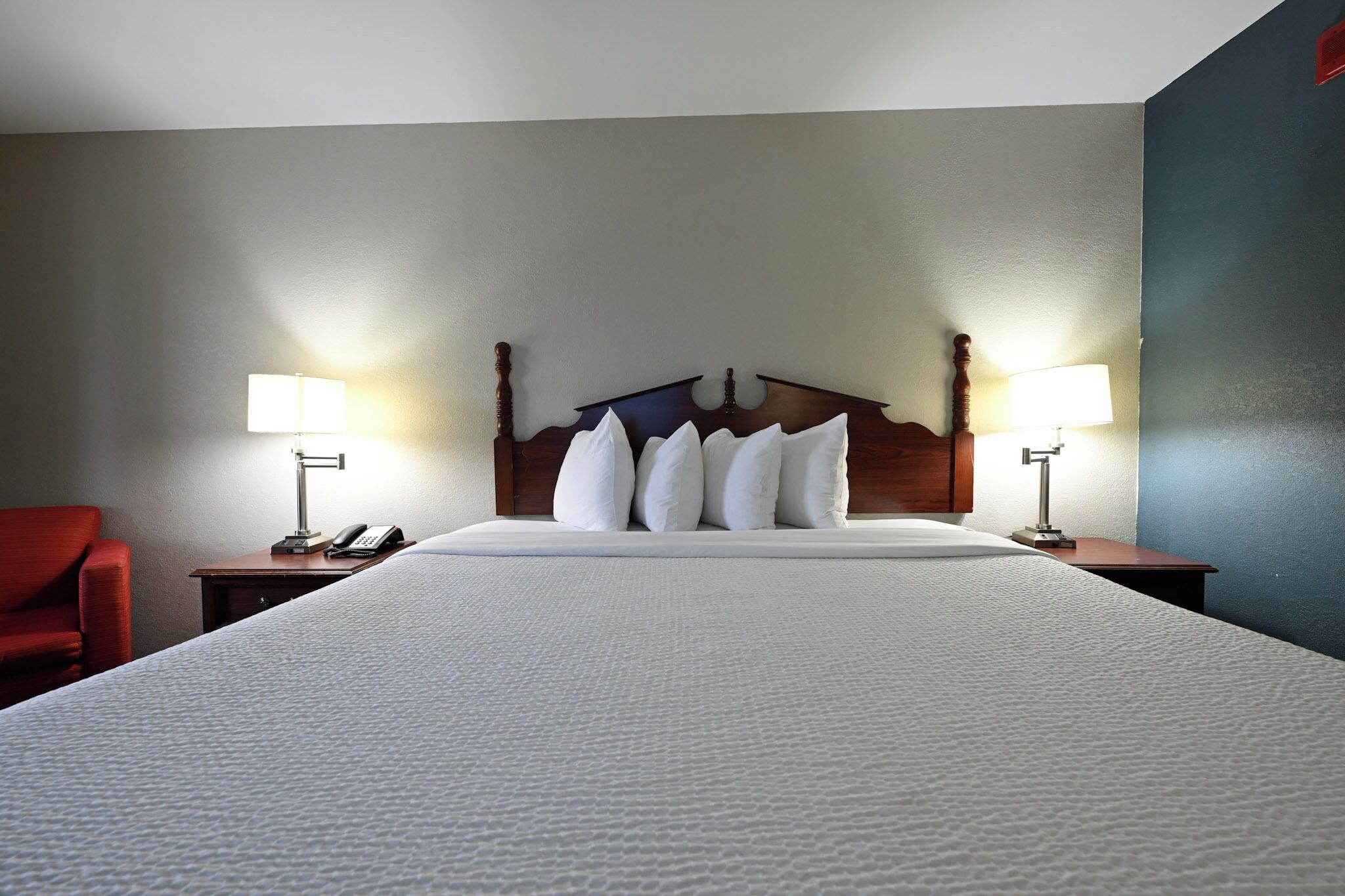 A hotel room with a large bed, two bedside tables with lamps, and a red chair.