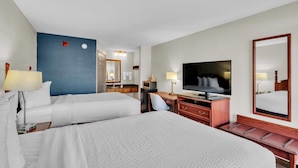 Habitación de hotel con dos camas, un escritorio, un televisor y un espejo grande.