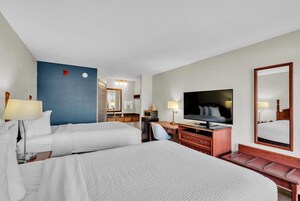 Habitación de hotel con dos camas, un escritorio, un televisor y un espejo grande.