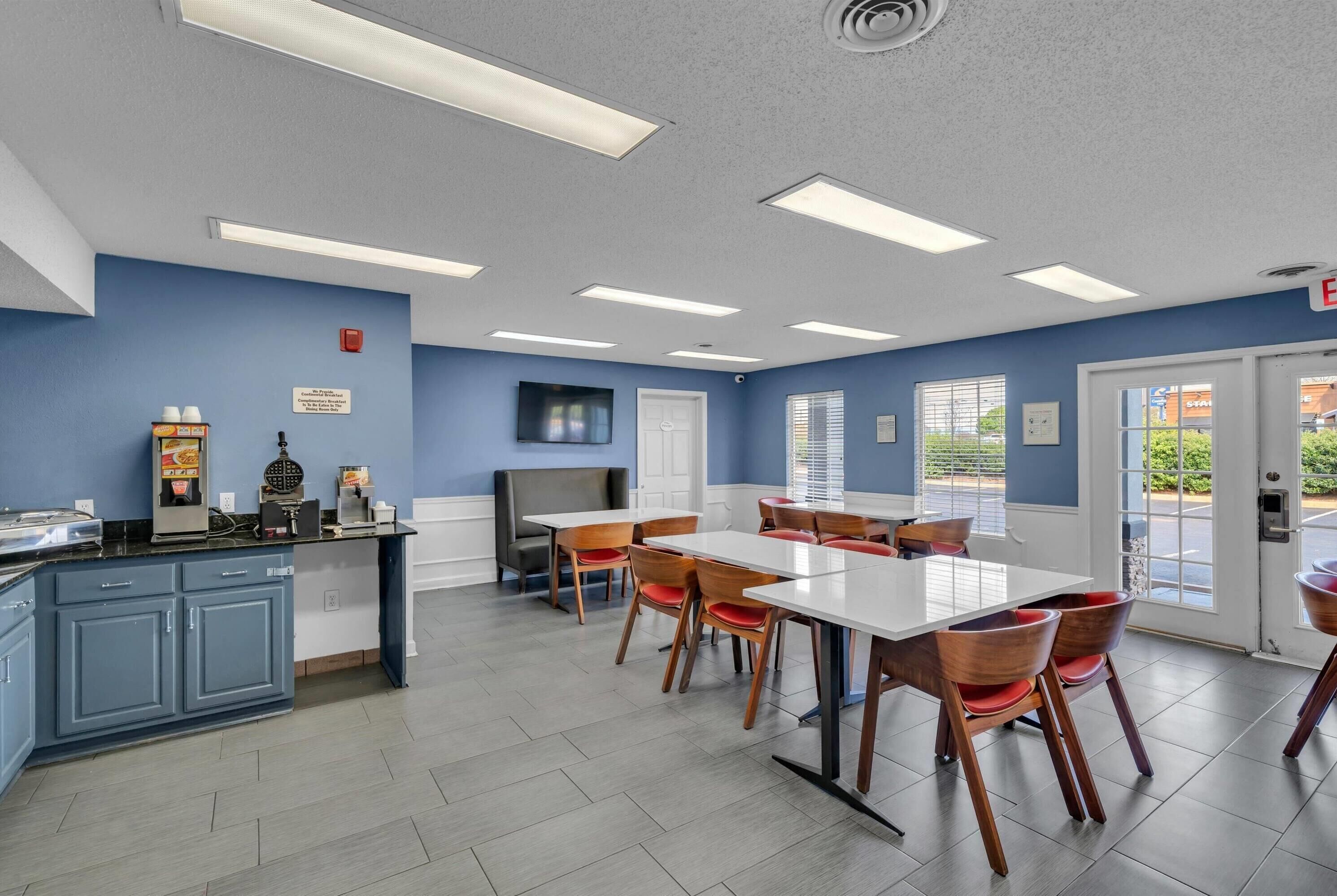 A restaurant with a blue wall, white ceiling, and a counter with food items. There are tables and chairs arranged for dining.