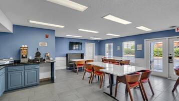 A restaurant with a blue wall, white ceiling, and a counter with food items. There are tables and chairs arranged for dining.
