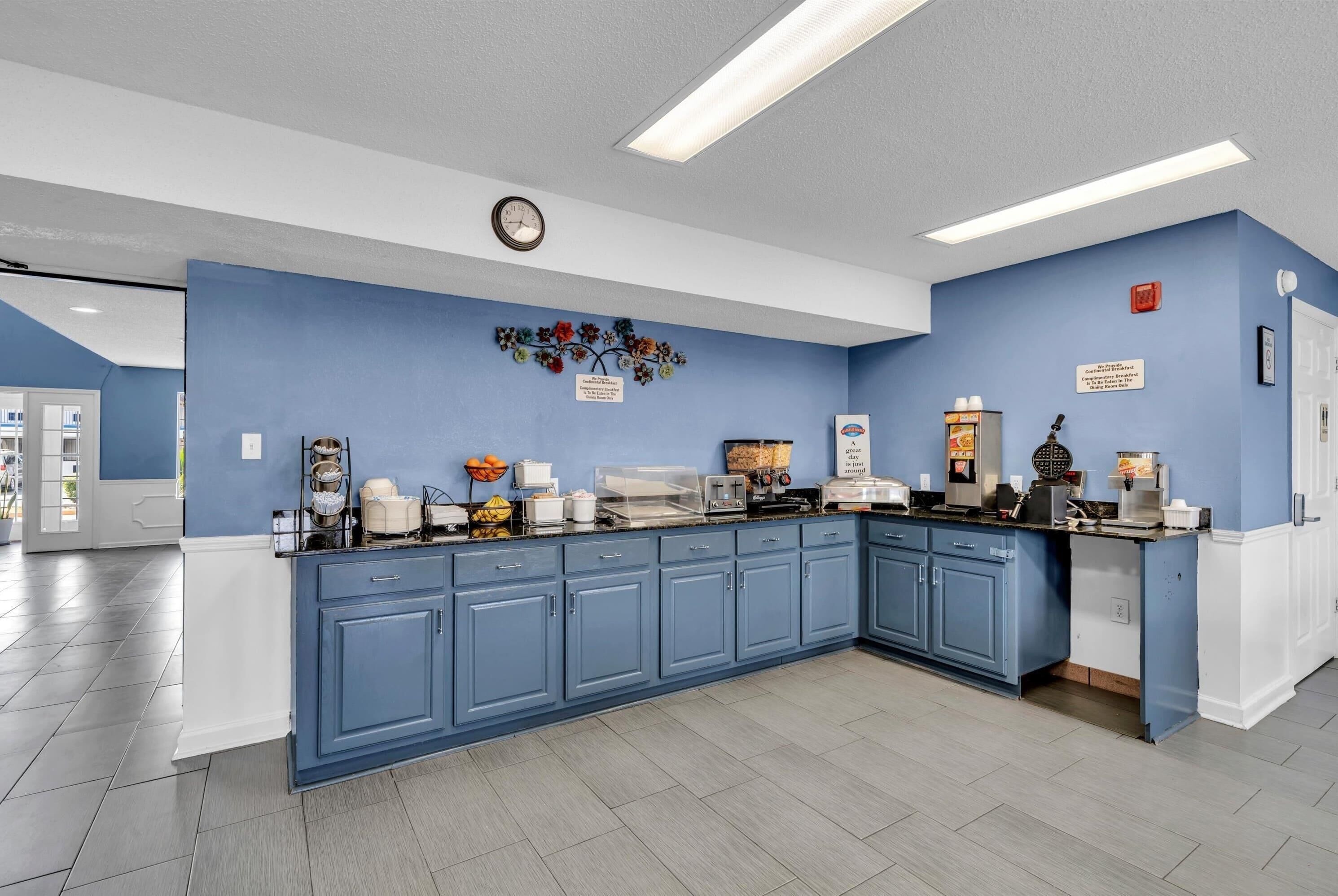 A kitchen with blue cabinets, a clock, and various appliances.