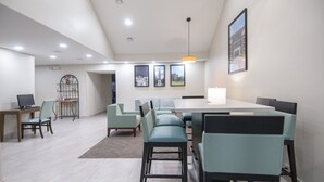 A modern dining area with a long table, multiple chairs, and a chandelier. - Baymont by Wyndham Tuscaloosa (Tuscaloosa)