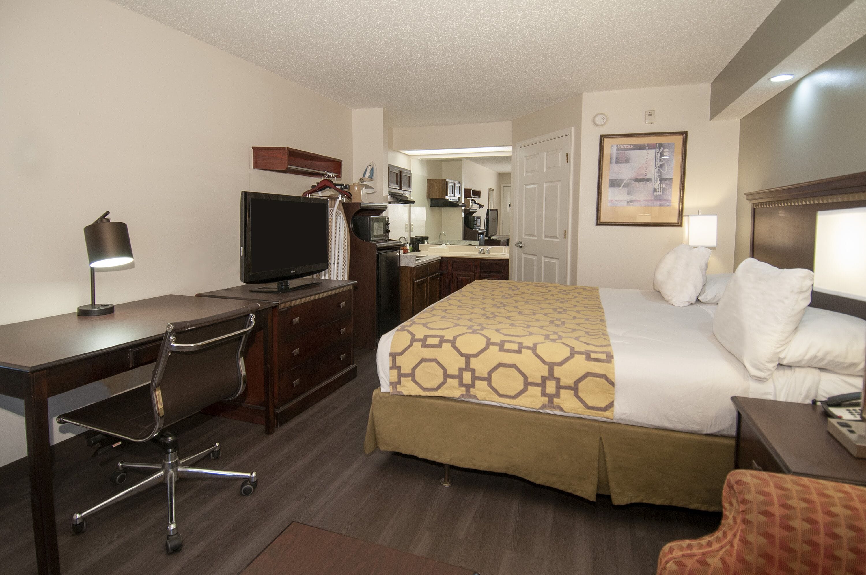 A hotel room with a bed, desk, chair, television, and a kitchenette.