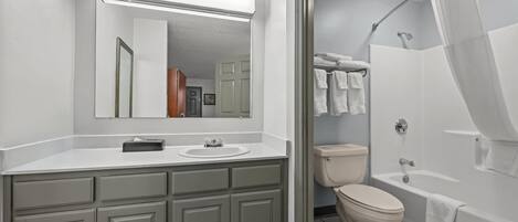 Une salle de bain avec un lavabo blanc, un miroir et des toilettes, ainsi qu’un espace douche séparé par un rideau.