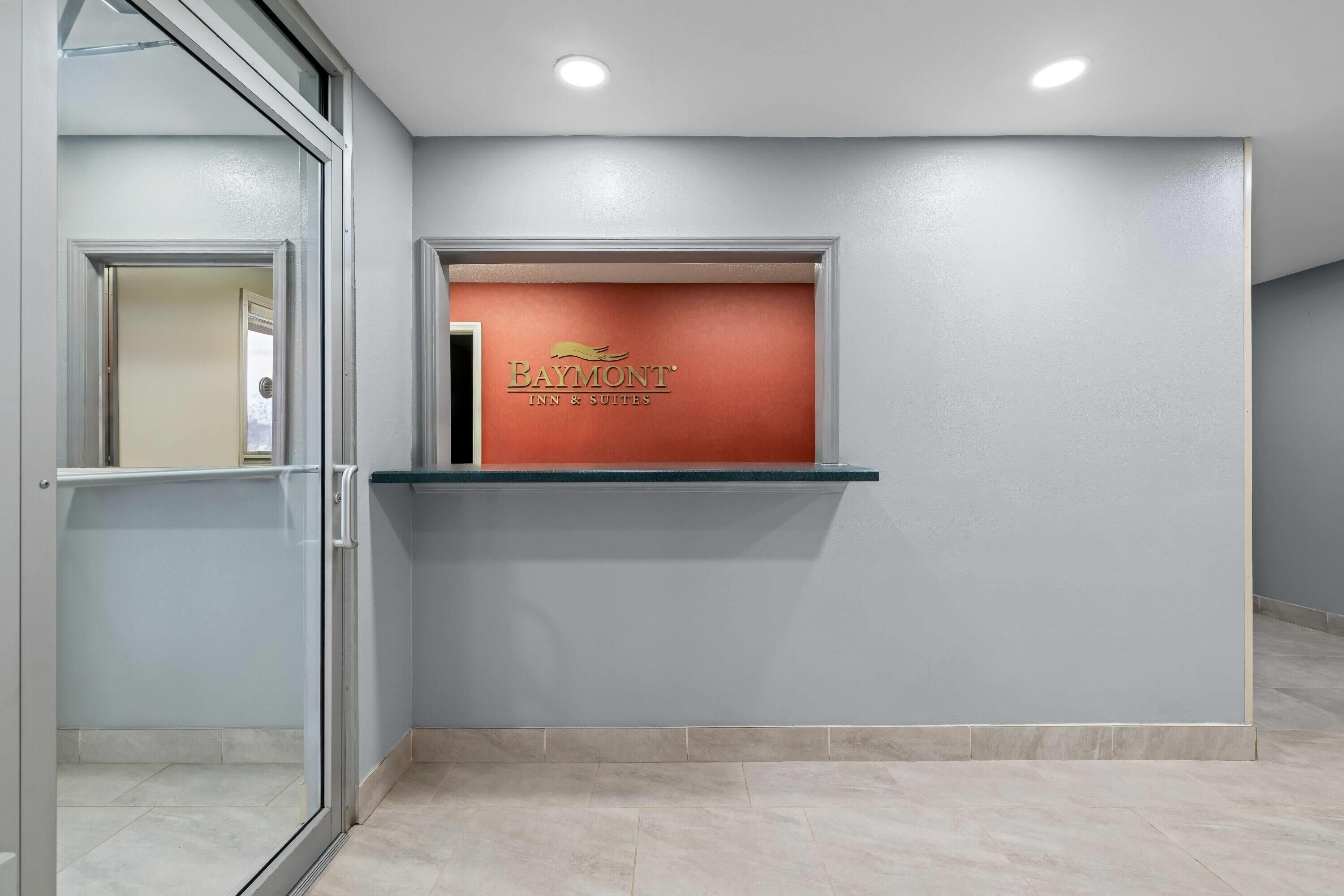 A reception area with a glass partition, a reception desk with a red backdrop, and a tiled floor.