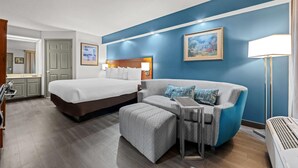 A hotel room with a large bed, a sofa, a small table, and a standing heater. - Baymont by Wyndham Tuscaloosa (Tuscaloosa)