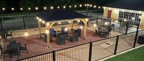 An outdoor patio area with a covered seating area, tables, and chairs, surrounded by a fence.