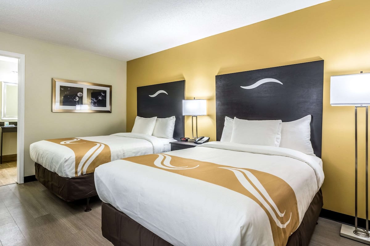 Quarto de hotel com duas camas, uma mesa de cabeceira, um abajur e um quadro na parede.