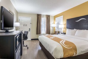A hotel room with a bed, a desk with a computer, a chair, a TV, and a window with curtains. - Quality Inn University Area (Auburn)