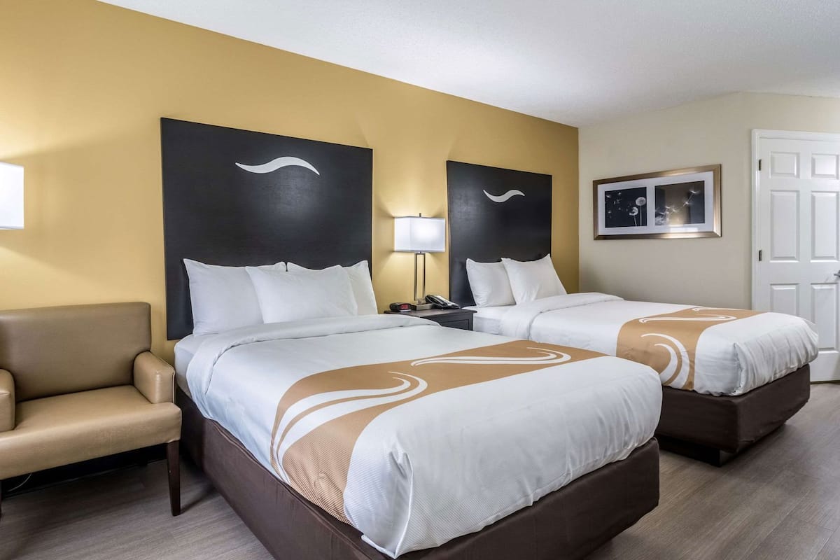Quarto de hotel com duas camas, um sofá, uma escrivaninha e um quadro na parede.