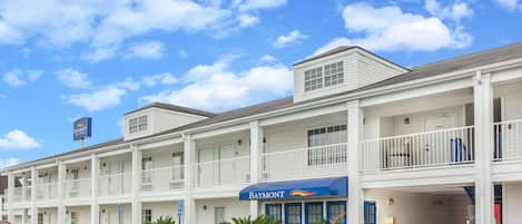 A multi-story motel with a blue awning, a parking lot, and a clear blue sky.