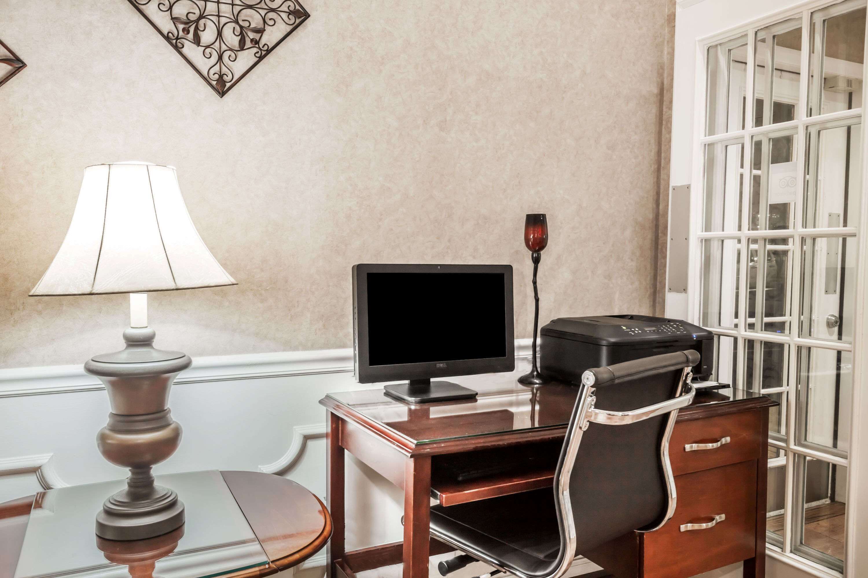 A hotel room with a desk, a lamp, a monitor, a printer, and a chair.