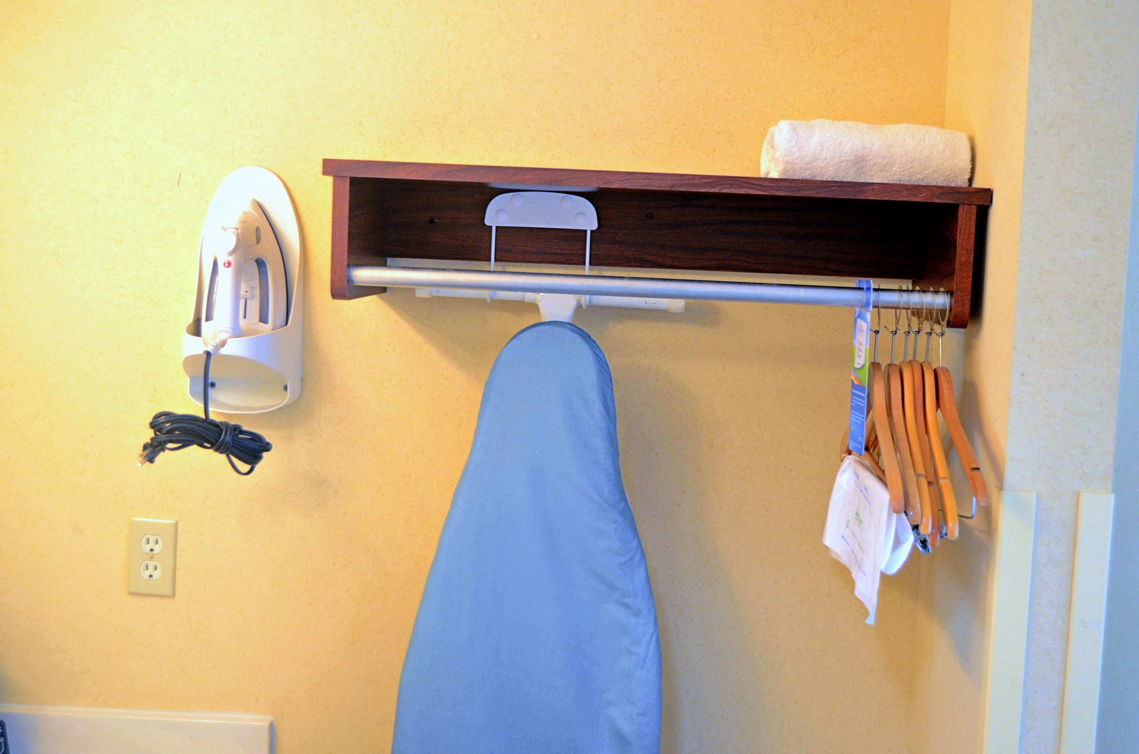 Un tablero de planchar fijado a la pared, con una plancha y un perchero encima.