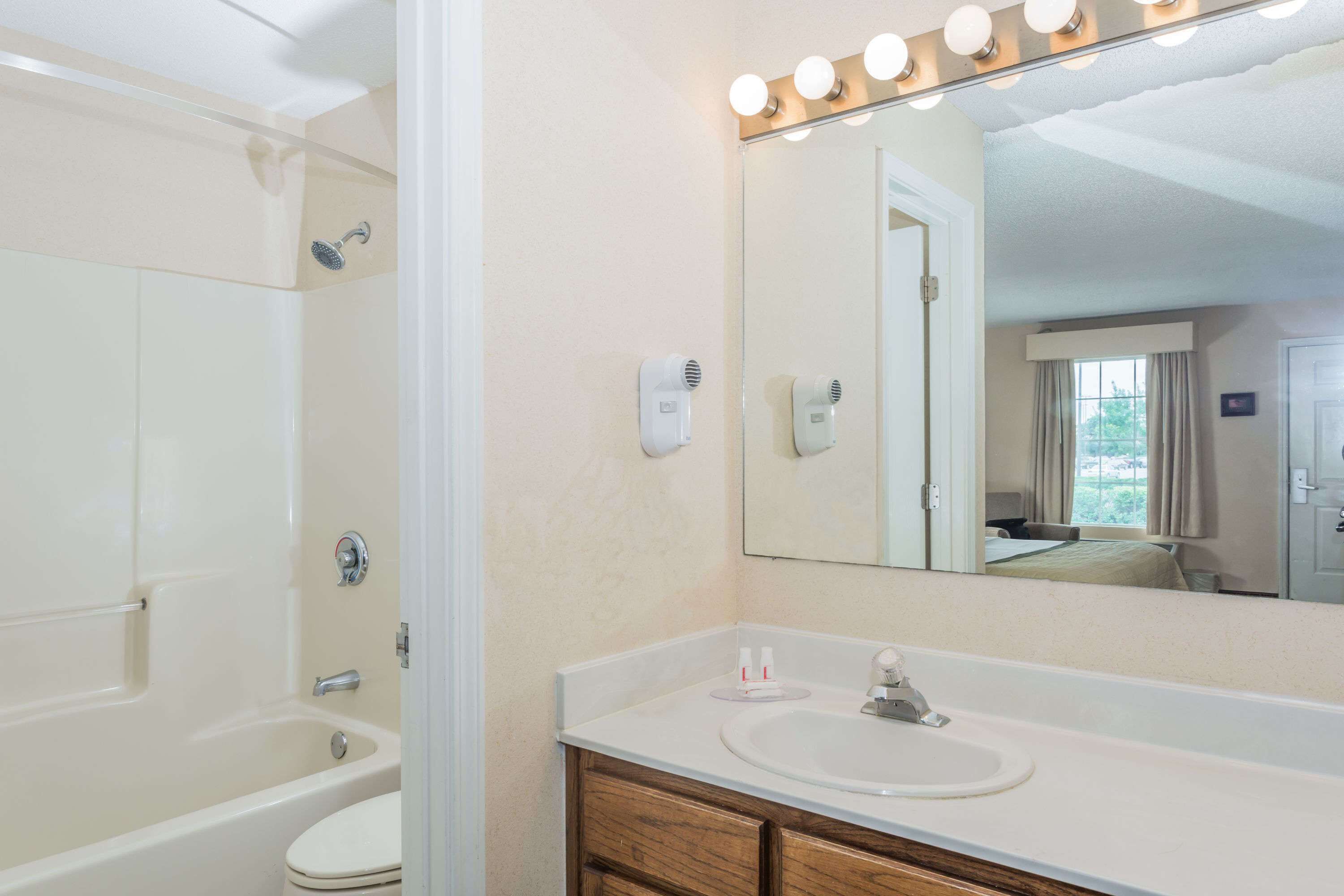 A bathroom with a bathtub, toilet, vanity with a sink, and a large mirror with lights.