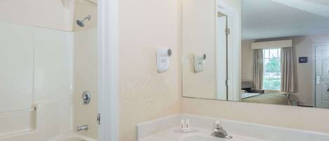 A bathroom with a bathtub, toilet, vanity with a sink, and a large mirror with lights.