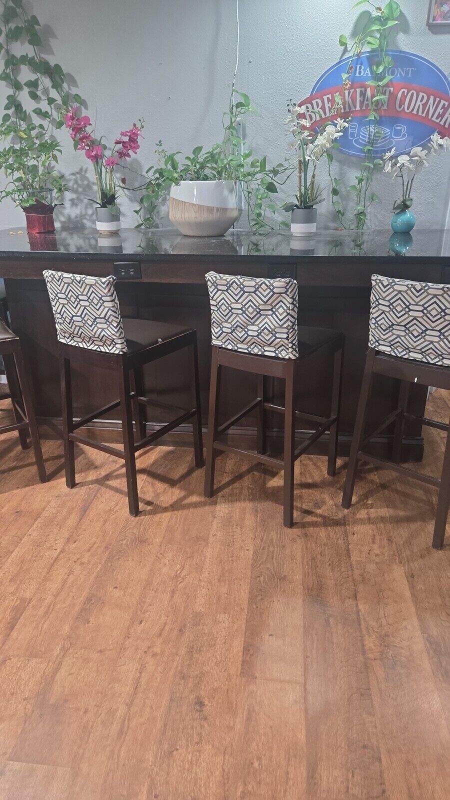 A breakfast bar with four chairs, a glass-top table, and potted plants.