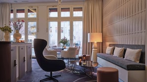Et moderne hotelværelse med et stort vindue, en sofa, en stol, et bord og en lysekrone.