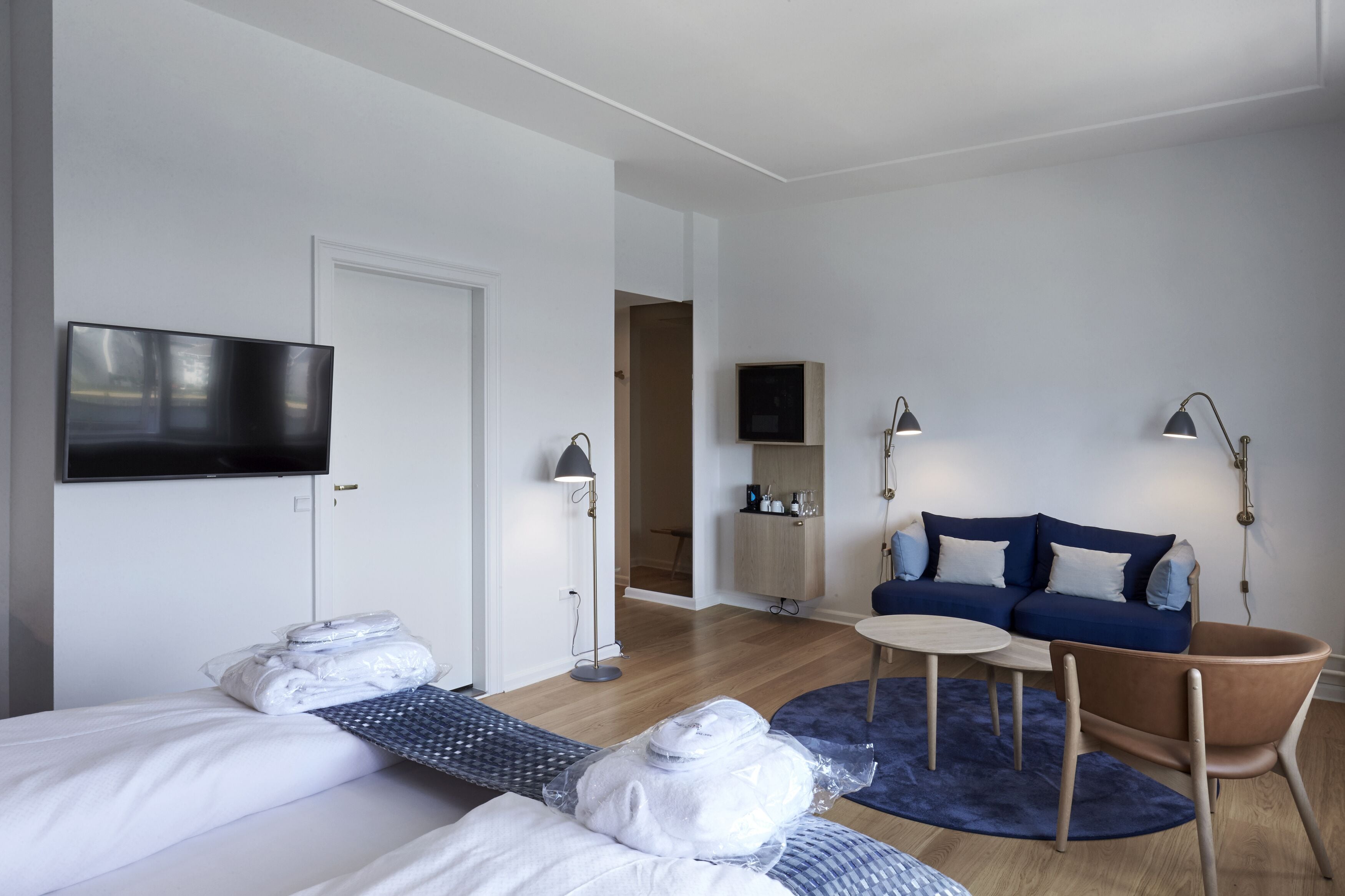 Quarto de hotel moderno com cama, sofá, televisão e uma pequena mesa.