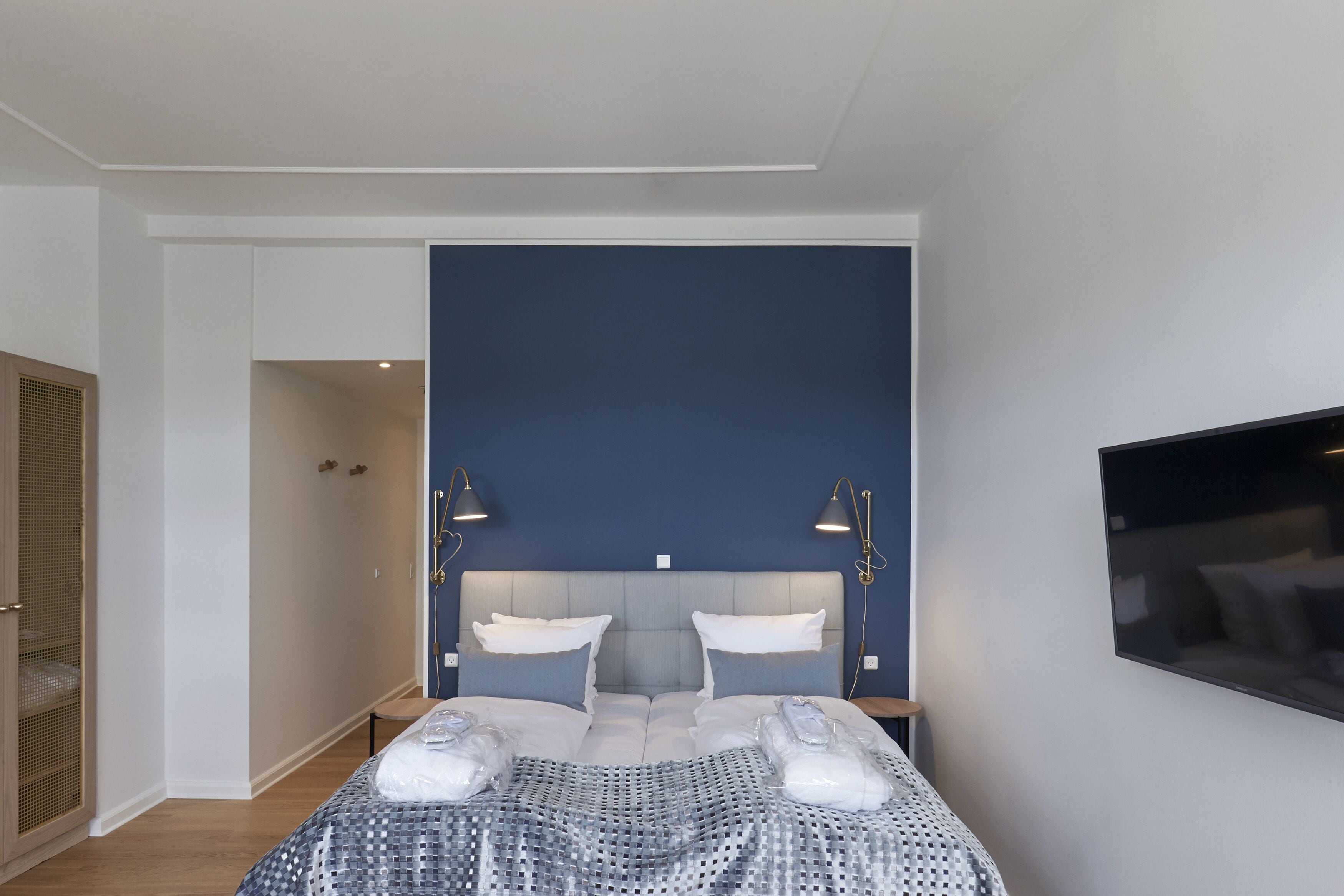 Een moderne slaapkamer met een groot bed, twee bedlampen, een televisie aan de muur en een kledingkast met spiegel.