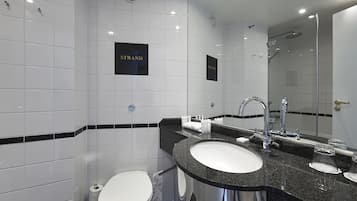 Un baño moderno con inodoro blanco, lavamanos con espejo y zona de ducha.