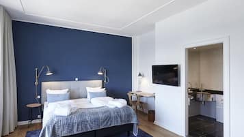 A modern bedroom with a large bed, bedside lamps, a desk, and a view into the bathroom.