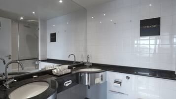 Un baño moderno con dos lavabos, cabina de ducha con mampara de vidrio y un inodoro.