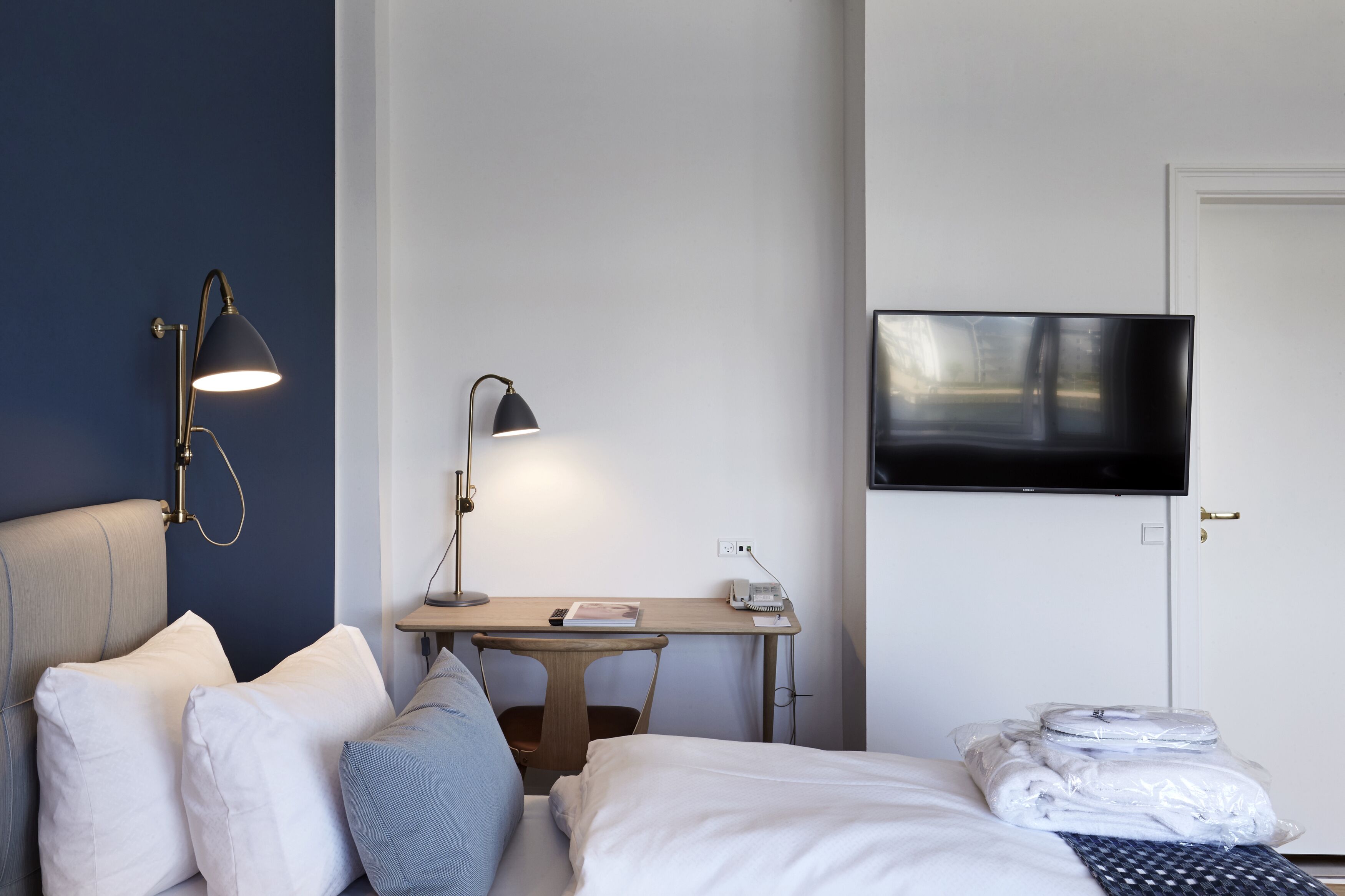Ein Hotelzimmer mit Bett, Kissen, Schreibtisch mit Lampe, Fernseher und einer Tür.