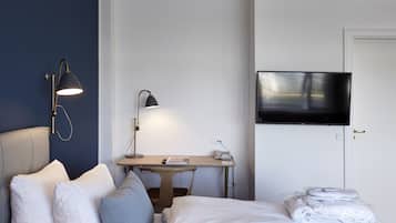 Ein Hotelzimmer mit Bett, Kissen, Schreibtisch mit Lampe, Fernseher und einer Tür.