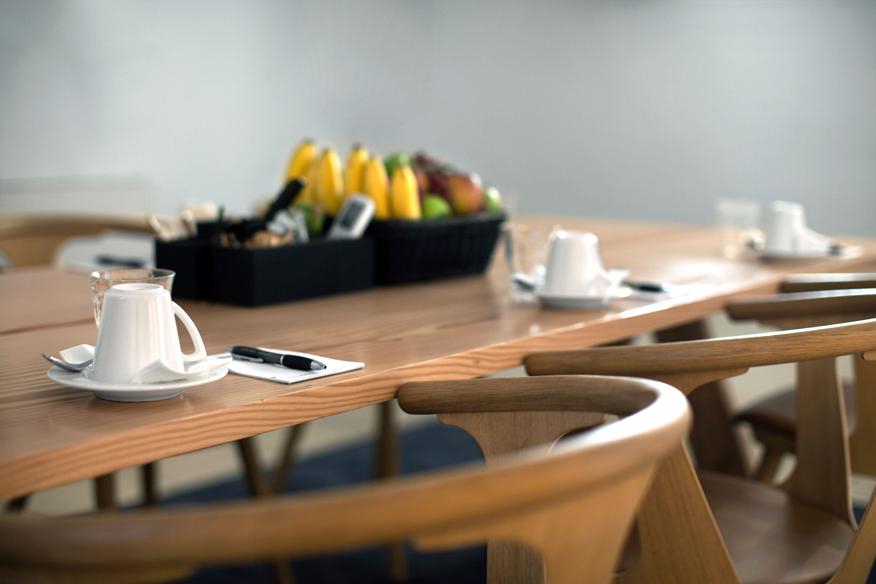 Una mesa de madera con una cafetera blanca, un teléfono inteligente y una cesta de fruta.