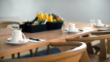 Una mesa de madera con una cafetera blanca, un teléfono inteligente y una cesta de fruta.