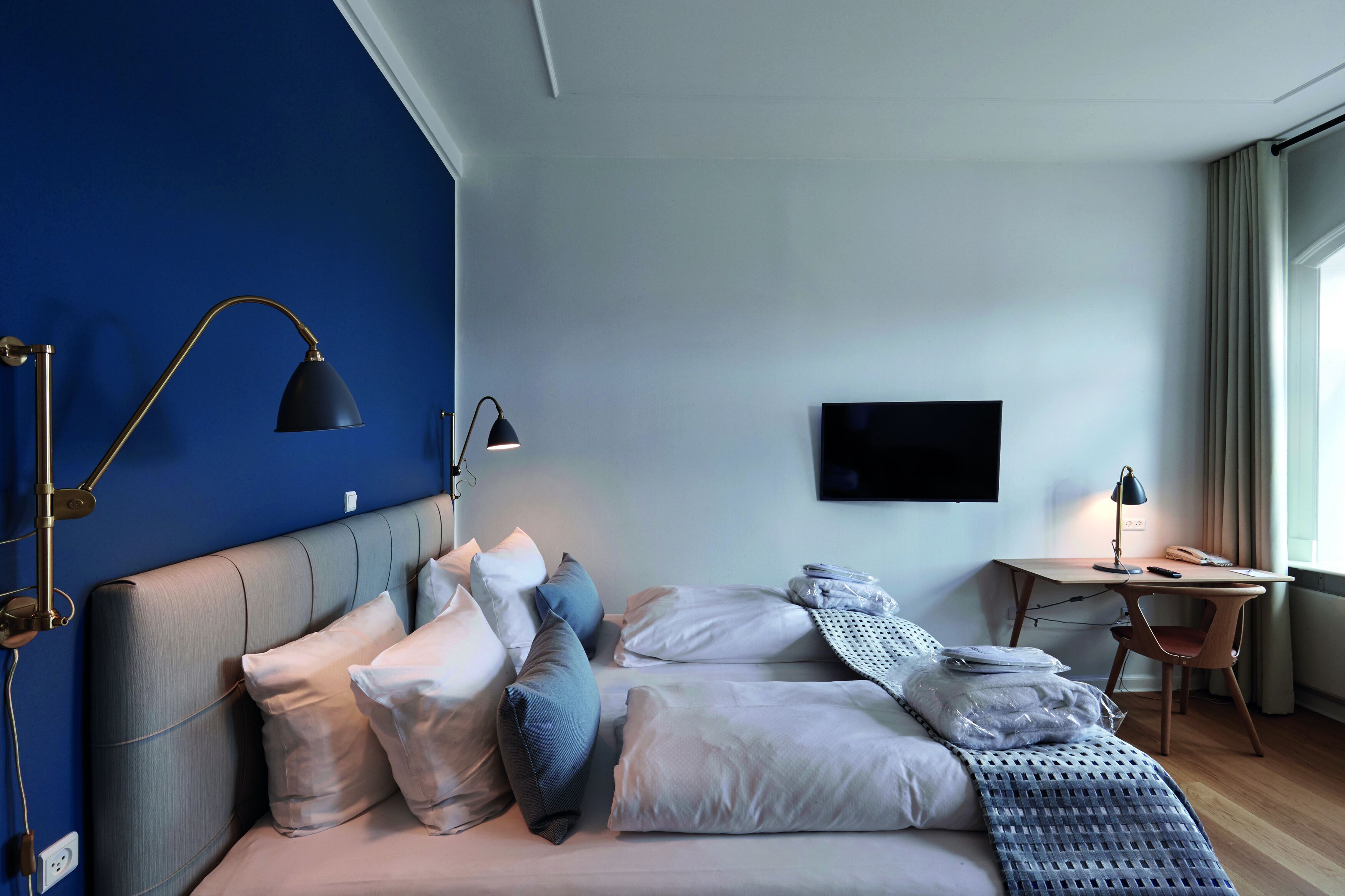 Una habitación de hotel moderna con cama, lámparas de noche, escritorio y televisión.