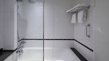 Un baño moderno con ducha envuelta en vidrio, una bañera y un perchero con toallas dobladas.
