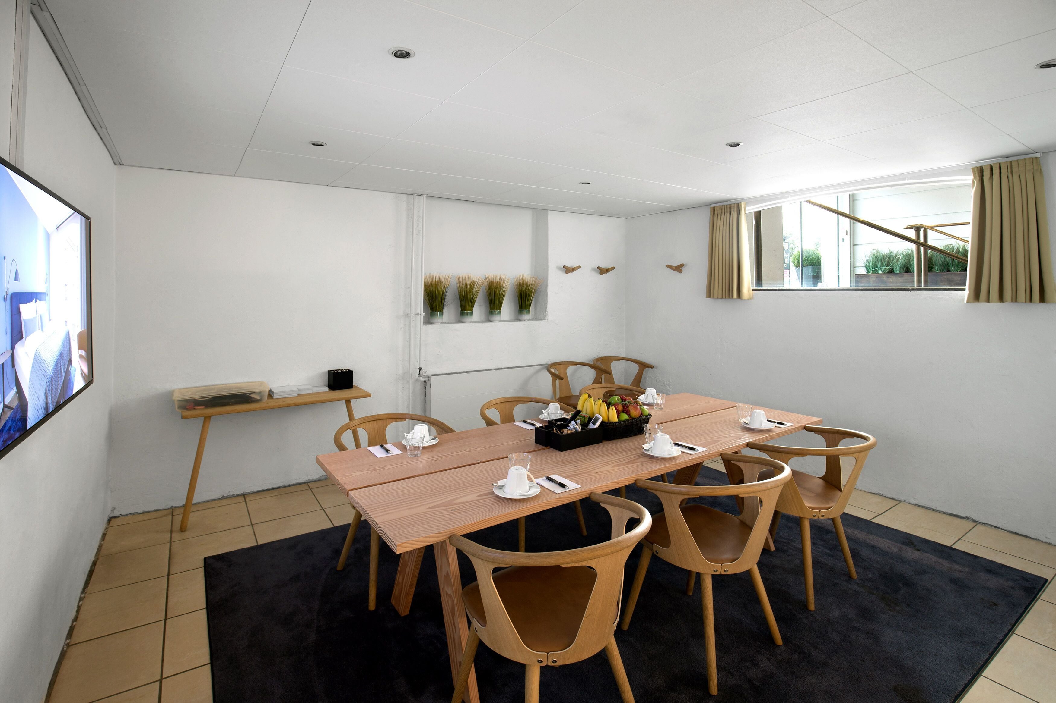 A conference room with a wooden table, six chairs, a black rug, and a window with curtains.