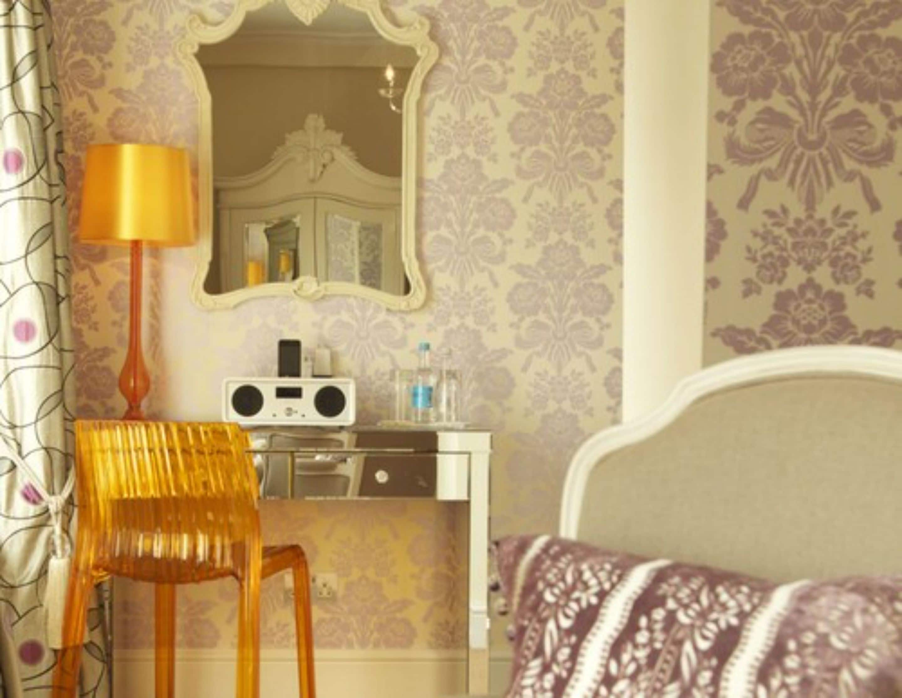A bedroom with a bed, a bedside table with a radio, a chair, and a mirror.