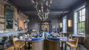 A restaurant with a brick wall, wooden tables, and blue cushioned seating.