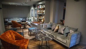 A modern living room with a grey sofa, orange velvet armchair, and two marble coffee tables.