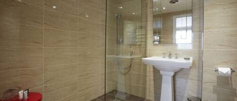 A modern bathroom with a glass-enclosed shower, a pedestal sink, and a red accent chair.