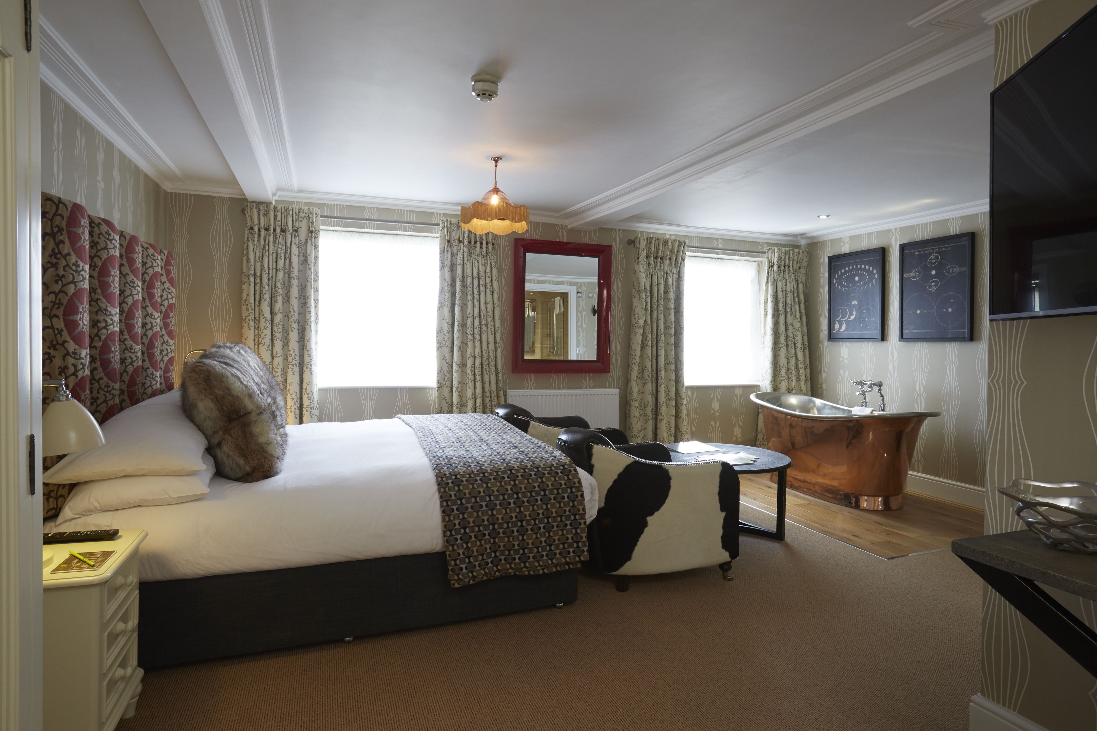 A hotel room with a large bed, a sitting area, a bathtub, and a television.